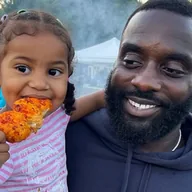 A dad holding his daughter while she eats a chicken skewer at a Saturday market (illustrative photo)